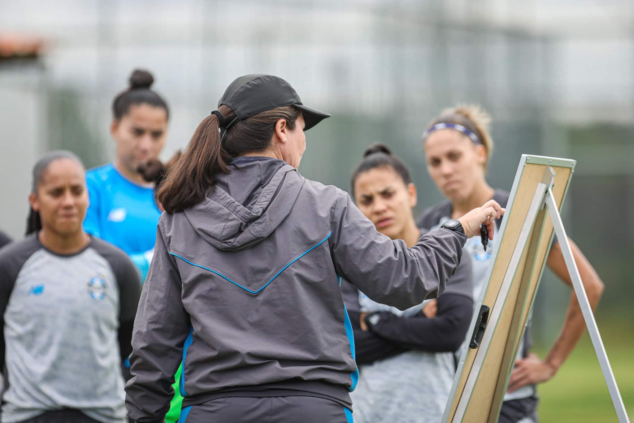 La entrenadora Jéssica de Lima explica técnicas de juego en un pizarrón a las jugadoras.